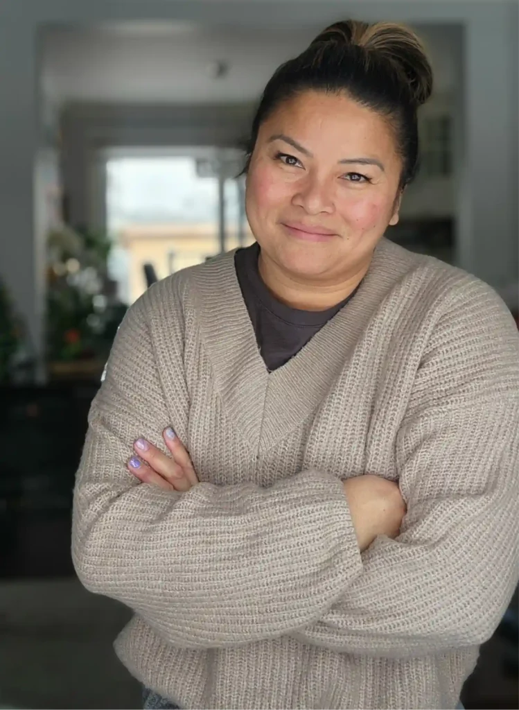 Dianne Jimenez standing with arms crossed facing, smiling wearing a beige-brown textured sweater